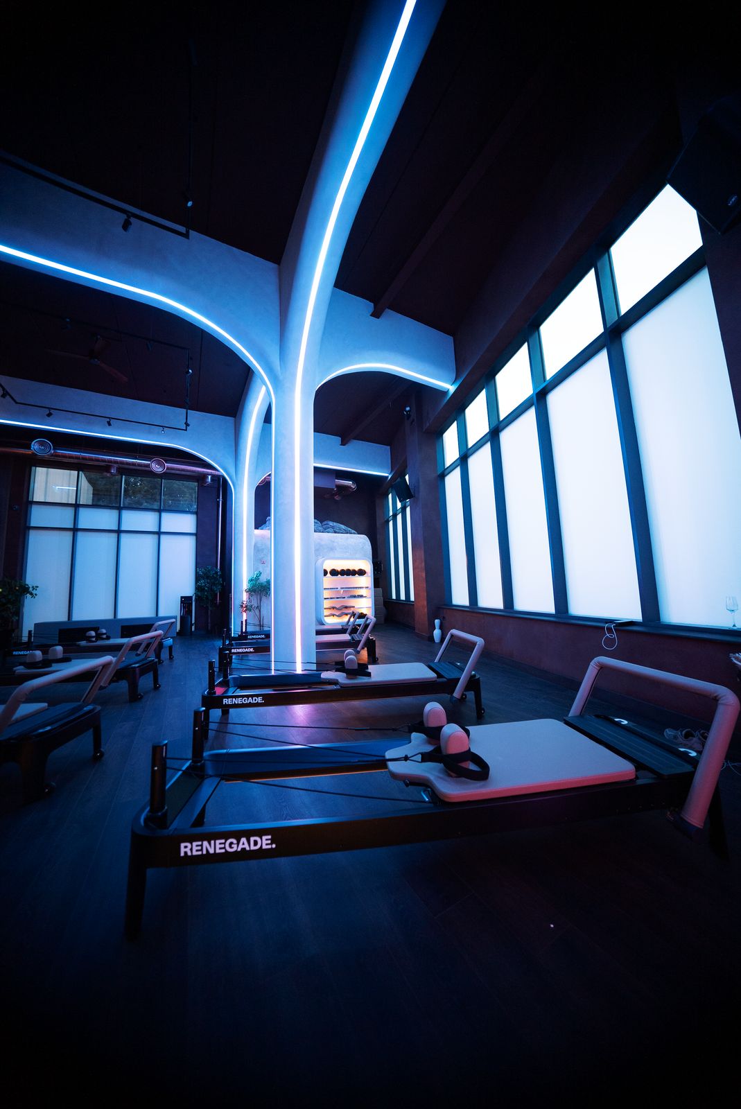 Renegade branded reformer machines lined up beneath a bright blue neon light pillar, next to the tall frosted studio windows at Renegade Reformer, Redfield, Bristol
