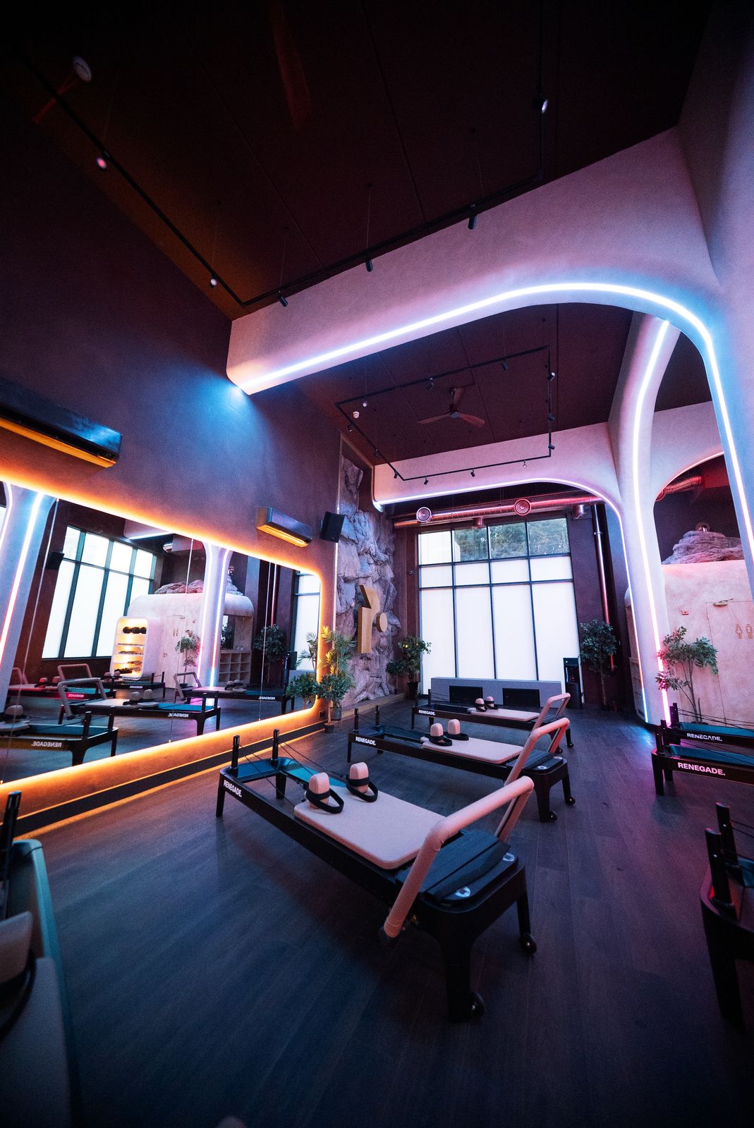 Renegade | By Night at Renegade Reformer, Bristol: the double height studio lit by curved blue and amber neon light arches running across the ceiling, with rows of reformer beds below