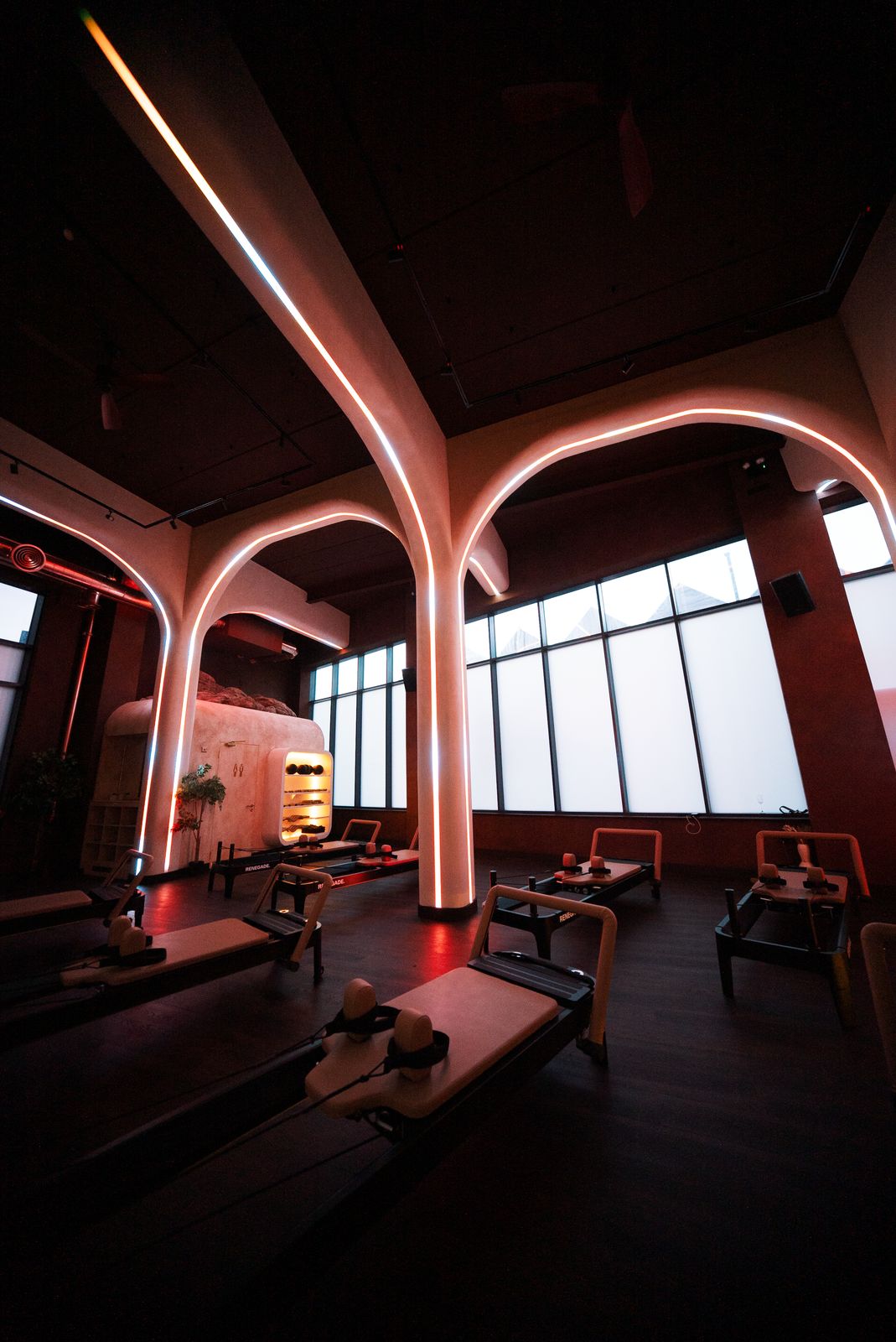 The Renegade Reformer studio washed in warm red and pink light, arched neon pillars glowing above reformer beds set up ready for an evening class