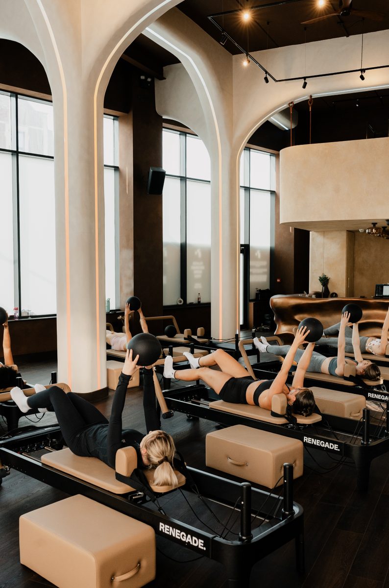 Wide view of a group reformer Pilates class at Renegade Reformer, Bristol, members using resistance bands and medicine balls beneath the studio's arched windows